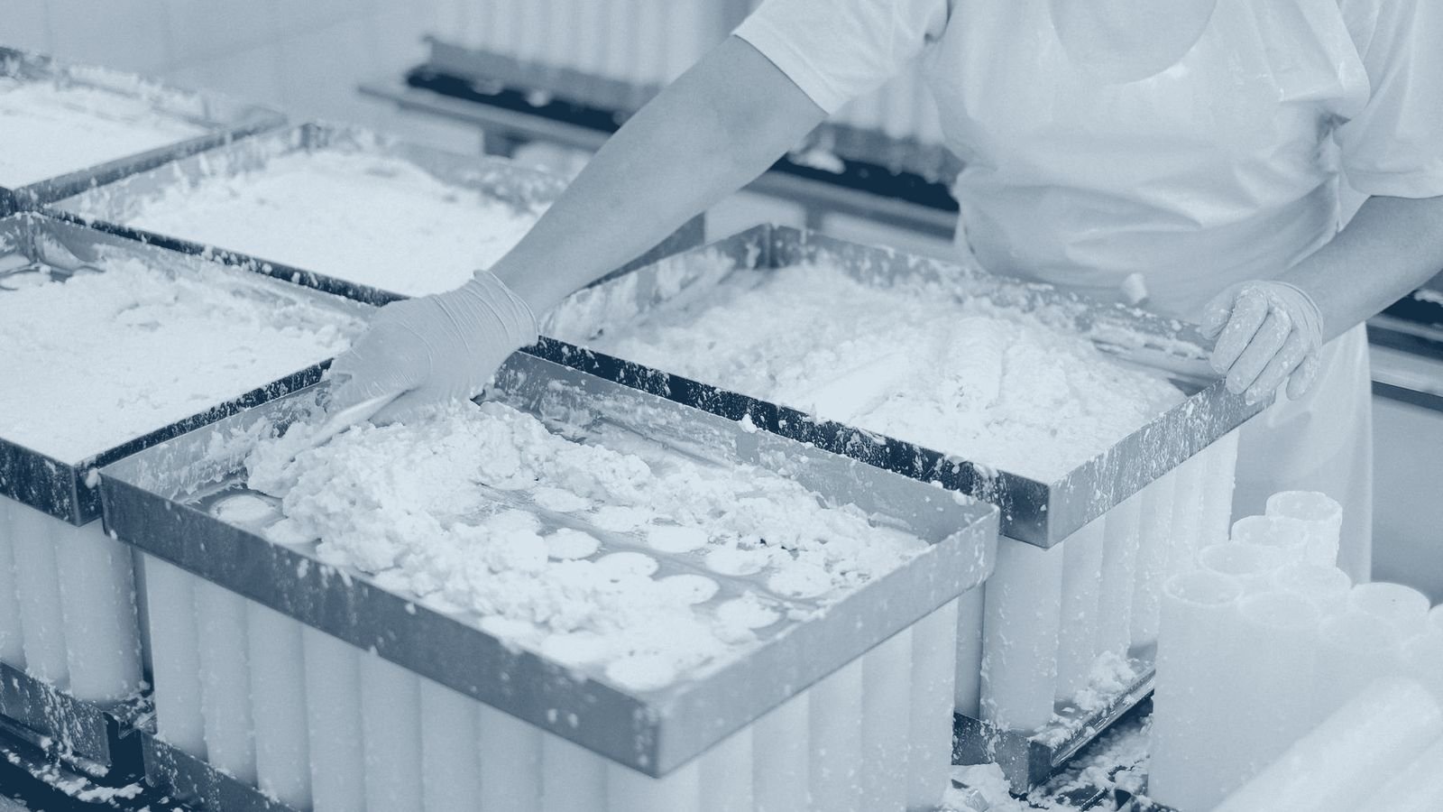 A worker in protective gear on a dairy production line